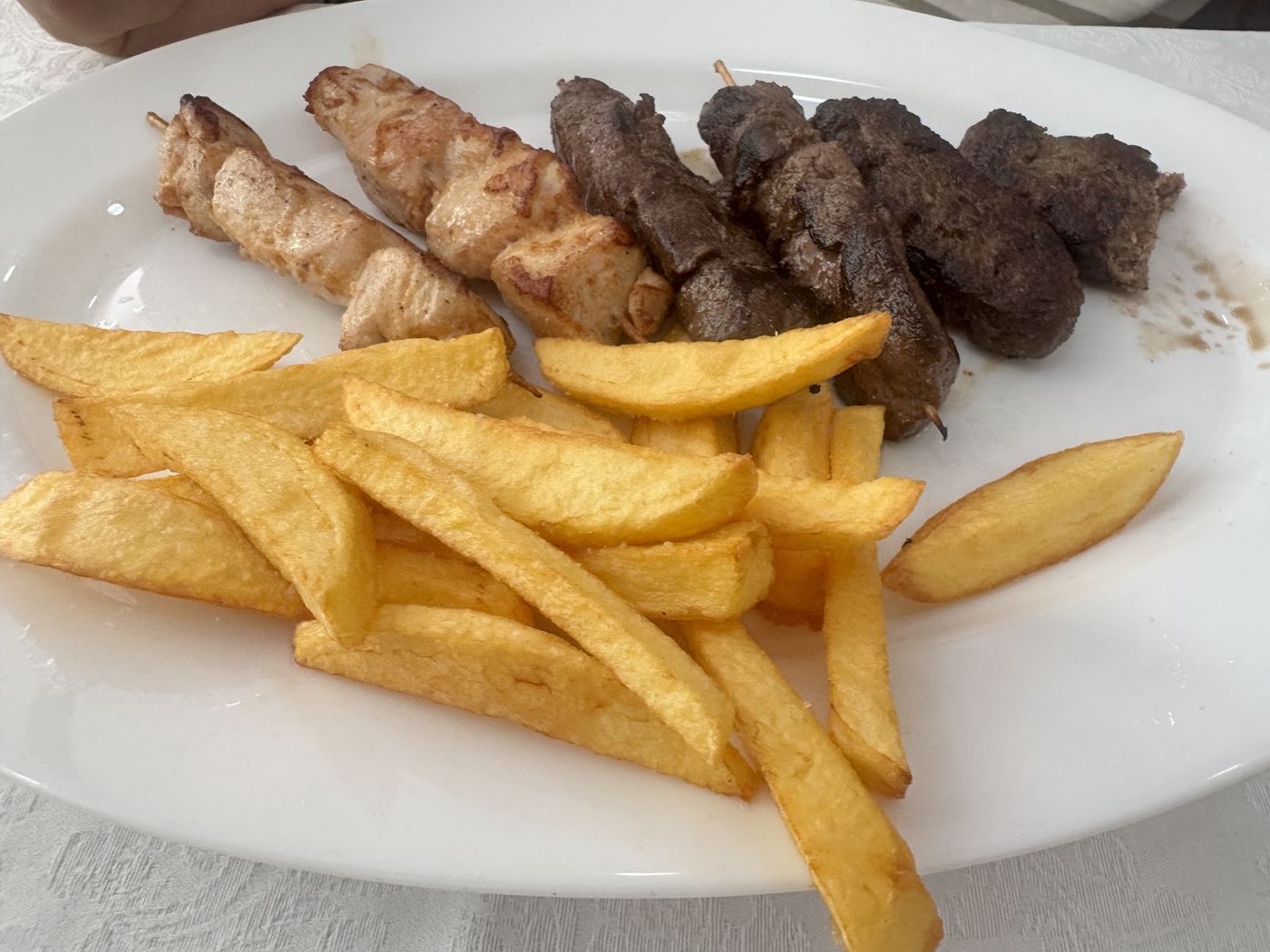 Pinchos mixtos de pollo y carne con patatas fritas a mano, plato principal de nuestra carta.